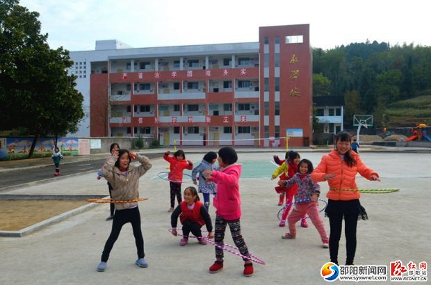 孩子們?cè)诓賵?chǎng)上開(kāi)心地玩著呼啦圈，背景為新建的教學(xué)樓