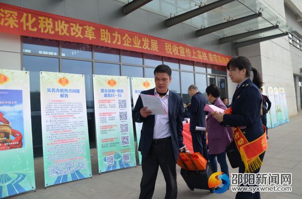 图为 进出高铁站的旅客阅读税收宣传资料