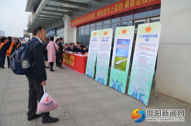 图为 进出高铁站的旅客驻足观看税收宣传展板