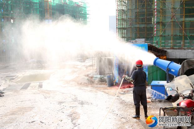 一处建筑工地内降尘保湿设备正在向空中喷射水雾，防止扬尘